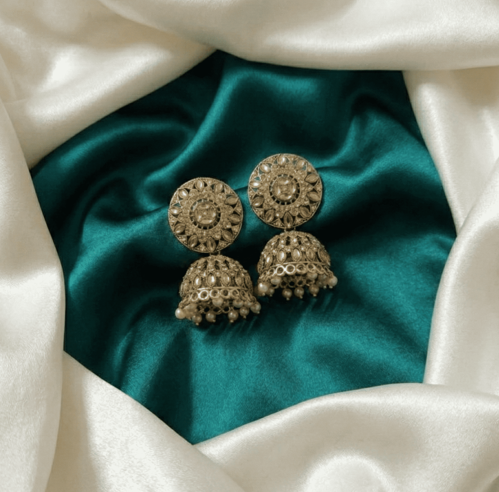 Pearl drop antique earrings on satin fabric background