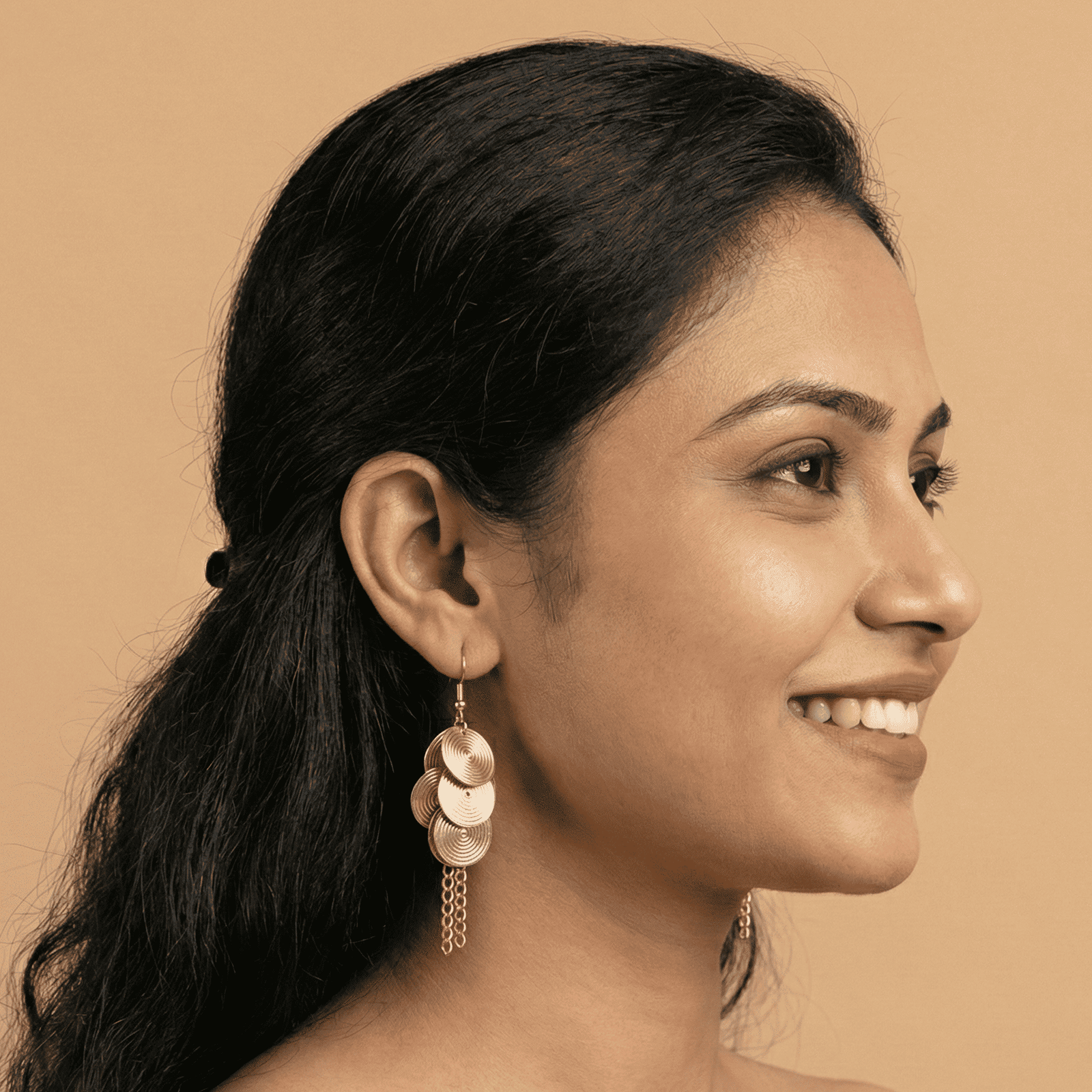 Side profile of woman wearing gold tone spiral disc tassel earrings with textured disc detailing
