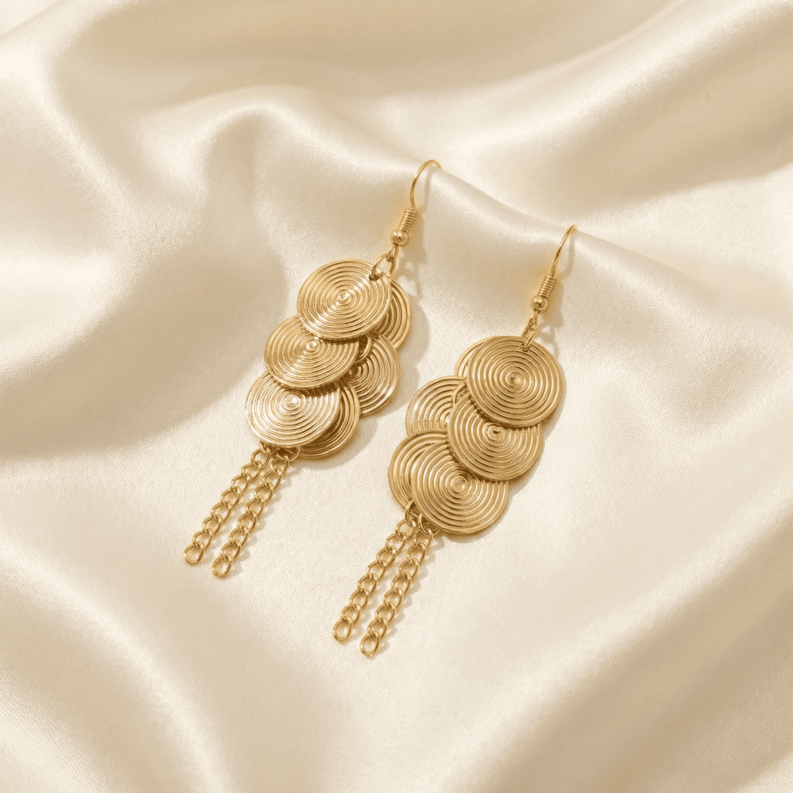 Gold tone spiral disc tassel fashion earrings for women displayed on soft ivory satin fabric