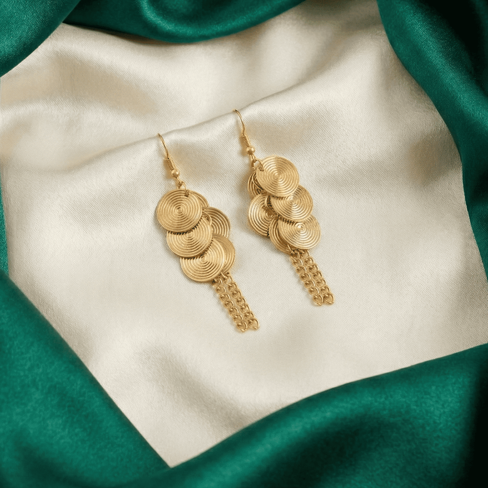 Fashion jewellery earrings with gold tone spiral discs and dangling chain tassels on satin background