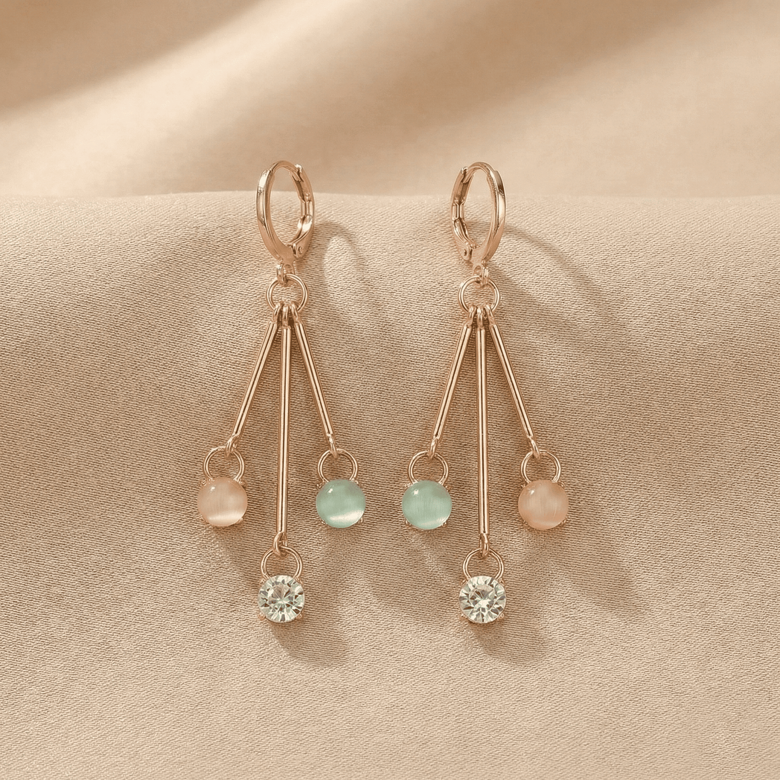 Trendy gold tone pastel drop earrings with crystal hanging charms on cream satin cloth