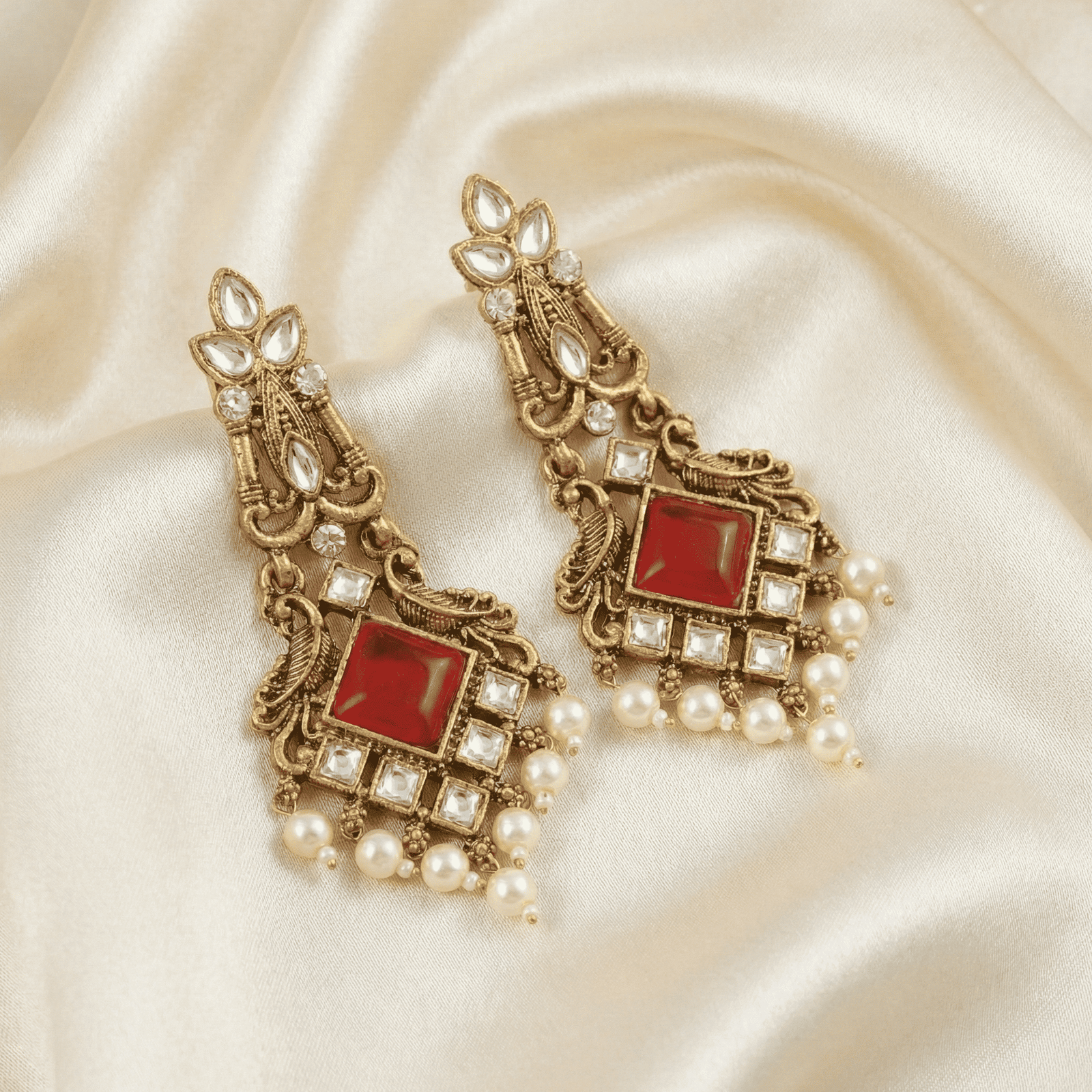 Close-up of antique gold kundan earrings featuring red centre stone and pearl bead hangings on ivory satin