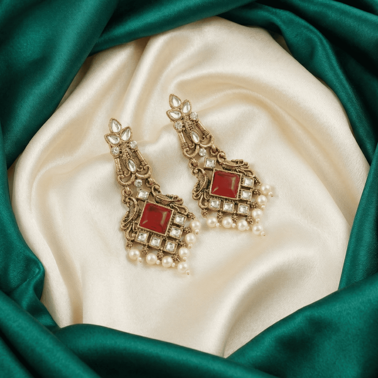 Red stone kundan pearl earrings for women displayed on cream satin with emerald green fabric border
