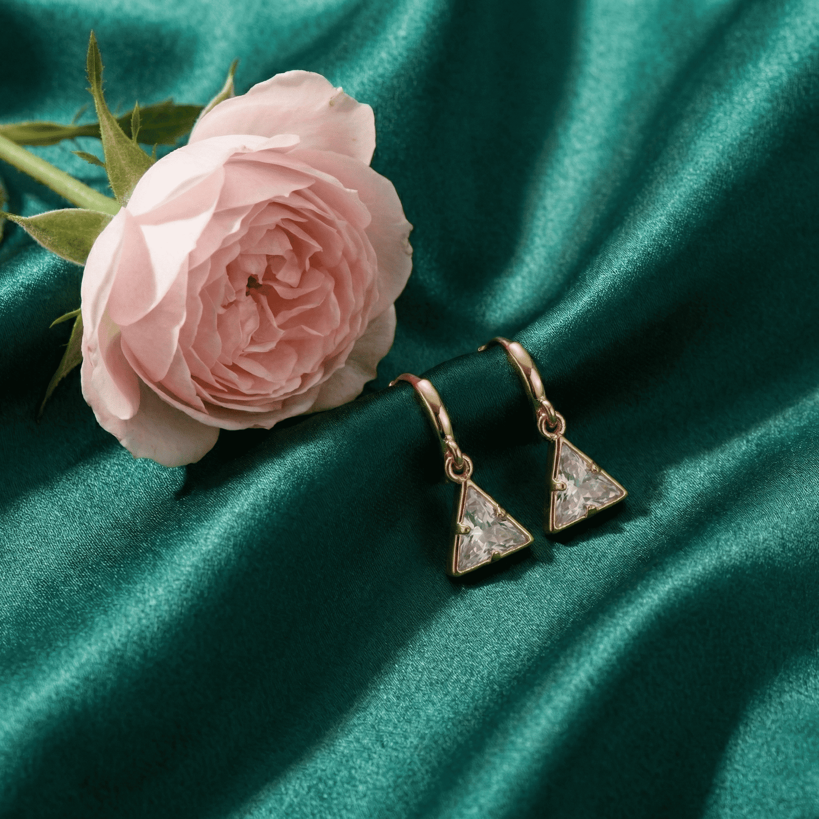 Trendy triangle earrings on green satin backdrop with pink rose styling