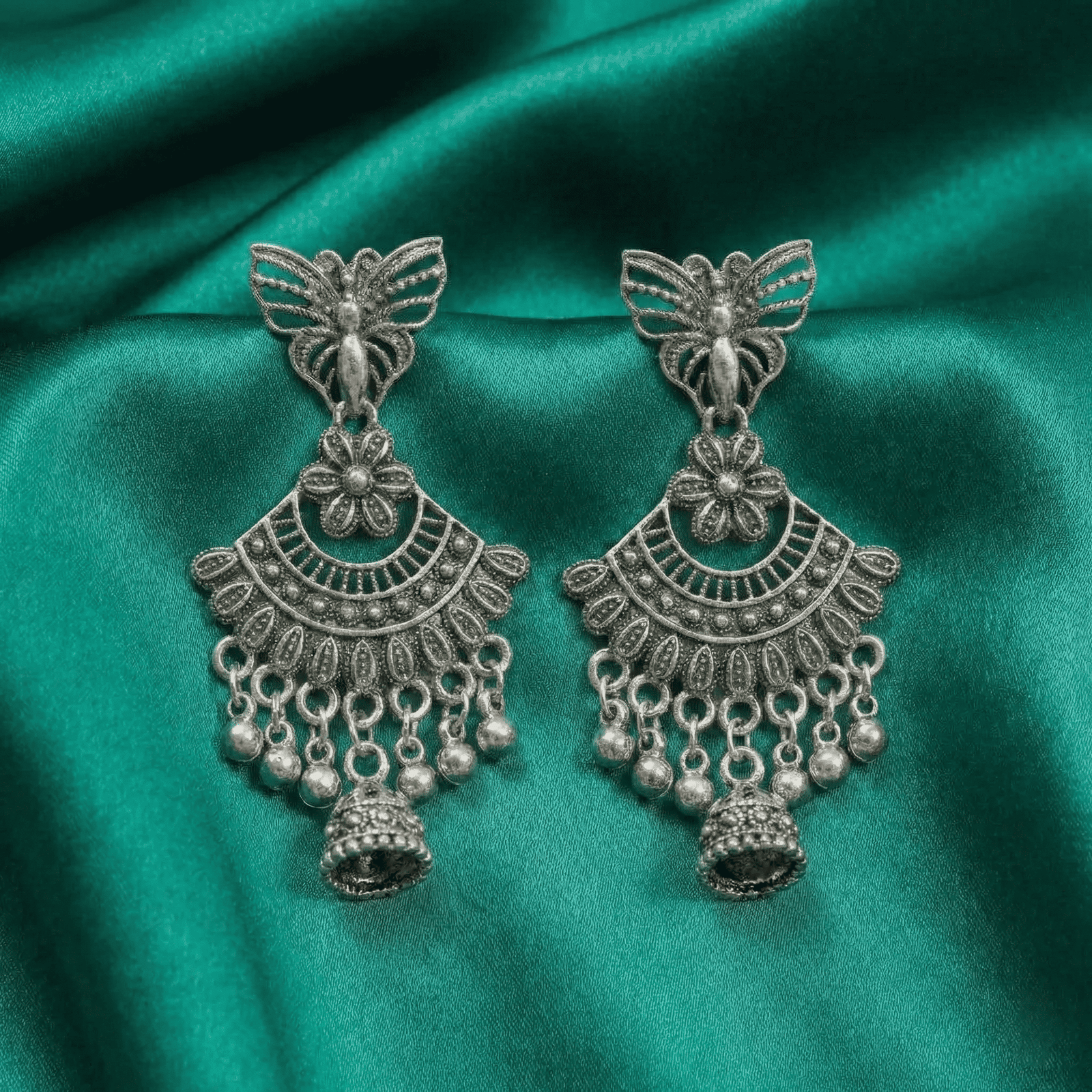 Butterfly-inspired oxidised silver jhumka earrings styled on satin fabric for ethnic and Indo-western outfits
