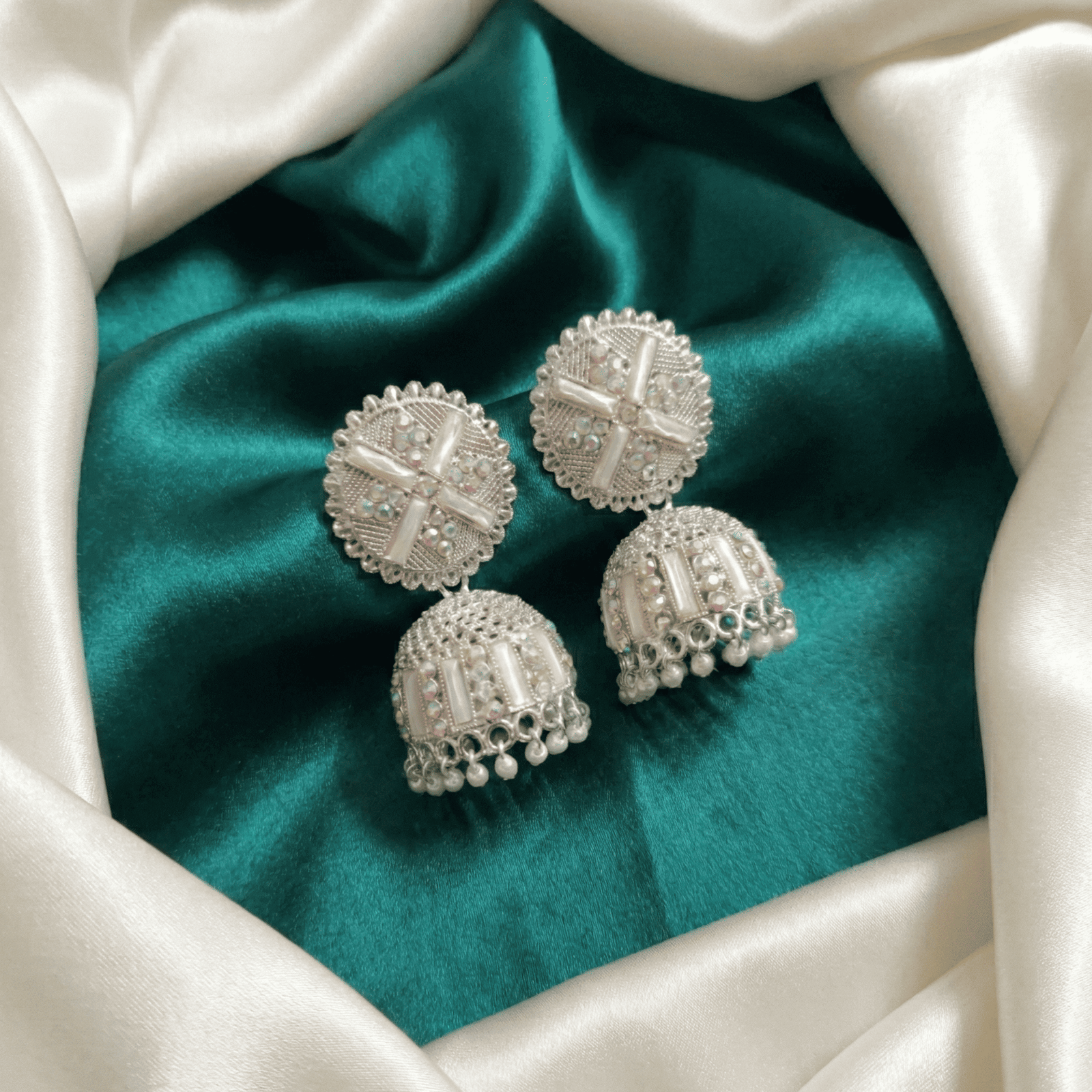 Party wear silver jhumka earrings on satin fabric background