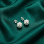 White pearl stud earrings for women on green satin fabric