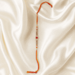 Eshanarya Royal Red Crystal Designer Rakhi with red and yellow thread on off-white satin background