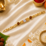 Lifestyle image of Eshanarya Gold Finish Om Bracelet Rakhi surrounded by diya, Rudraksha, rice, flowers and festive Raksha Bandhan decorations.