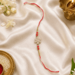 Festive flat lay of Red Crystal Snowflake Designer Rakhi with diya, kumkum, and rice