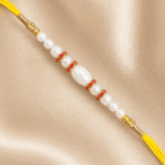 Eshanarya Pearl Designer Rakhi with White Pearl Beads, Yellow Sacred Thread and Gold-Tone Accents on Soft Satin Background