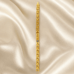 Vertical View of Eshanarya Gold Bracelet Style Rakhi with Blue Crystal Accent on Satin Background