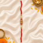 Designer crystal rakhi with floral motif, pearl detailing, and festive red thread on satin fabric