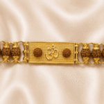 Close-up of gold-tone Om bracelet rakhi with textured centre plate and authentic rudraksha beads