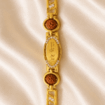 Eshanarya Mere Bhai Bracelet Rakhi with crystal-studded oval centreplate, Rudraksha beads and gold finish bracelet links on satin background