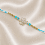 Angled close-up of Eshanarya Sky Blue Crystal Snowflake Designer Rakhi on satin background