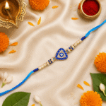 Blue Evil Eye Triangle Designer Rakhi displayed with diya, kumkum, flowers and festive décor for Raksha Bandhan celebrations.
