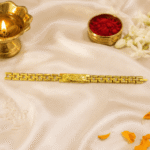 Eshanarya gold finish Bracelet Rakhi displayed with diya, kumkum, rice, jasmine flowers and marigold petals for Raksha Bandhan