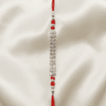 Vertical Close-up of silver crystal Rakhi featuring multi-row crystal detailing and red bead accents