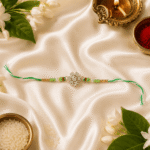 Designer green crystal Rakhi with festive diya kumkum rice and jasmine flowers for Raksha Bandhan